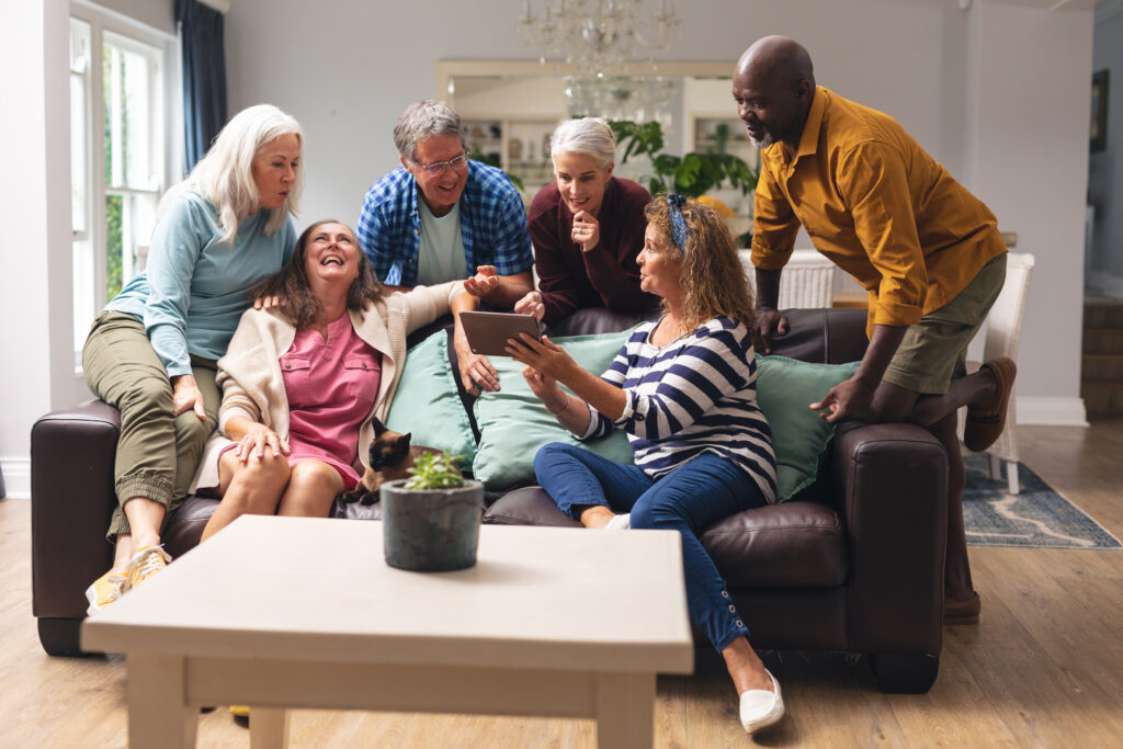 Happy multiracial senior male and female friends looking at digital tablet at home. unaltered, lifestyle, friendship, leisure, domestic life, social gathering and togetherness.